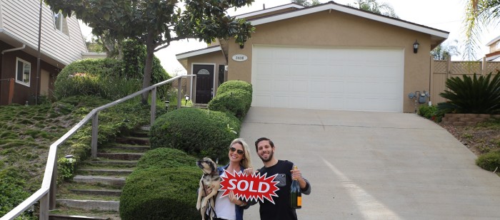 Happy couple holding "Sold" sign and champagne in front of new home